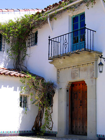A Spanish style wood front door with cut stone door surround and iron balcony above it. Photo taken at Casa del Herrero estate in Montecito, California